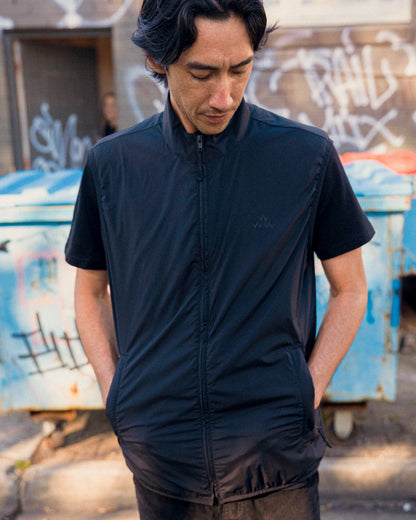 A man wearing a black shell vest with a funnel neck and a tonal chest print, outdoors.