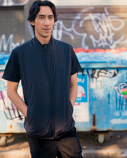 A man wearing a black shell vest with a funnel neck and a tonal chest print over a black t-shirt.