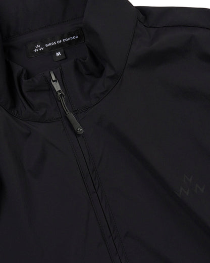 Detail of a black vest with a funnel neck, full zip, and a tonal left chest triple eagle print.