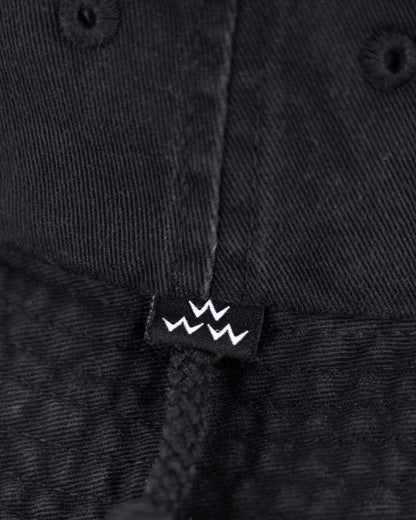 Detail of a black cotton boonie hat showing a small black label with three white crown icons.