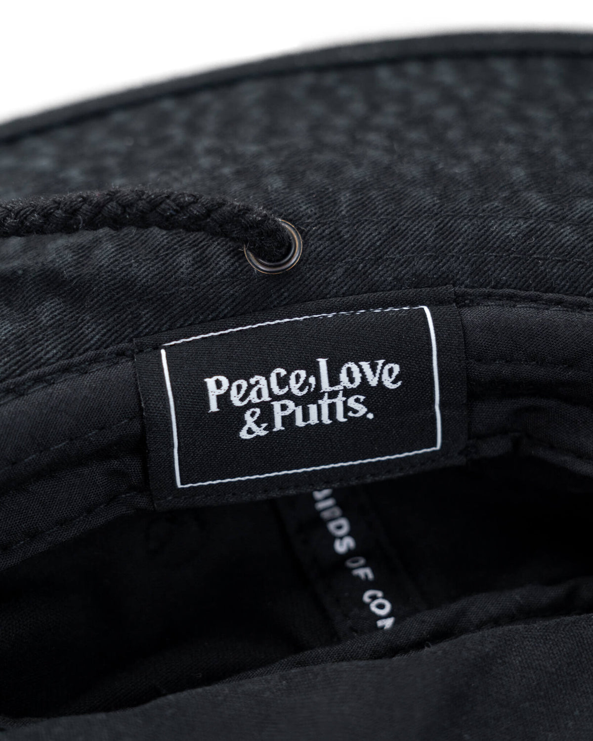 Detail of the interior label on a black cotton boonie hat reading Peace, Love & Putts inside the brim.