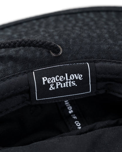 Detail of the interior label on a black cotton boonie hat reading Peace, Love & Putts inside the brim.