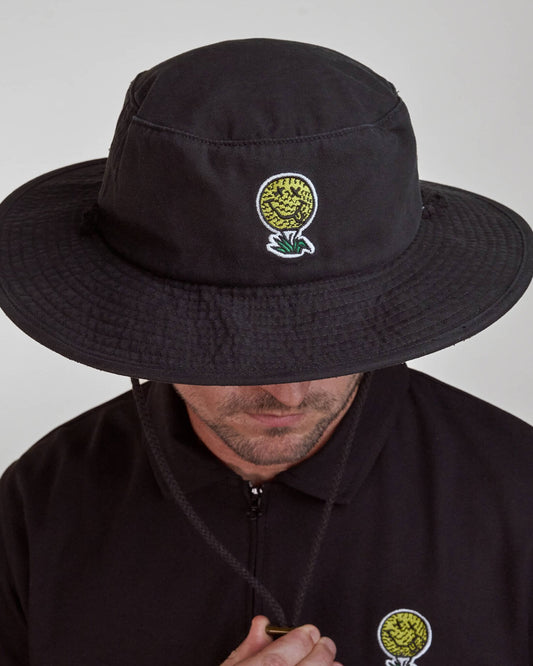 A man wearing a black boonie hat with a yellow and white smiley face golf ball design on the front.