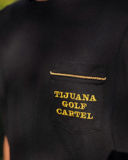 Detail of a black t-shirt featuring a chest pocket with gold twisted rope trim and embroidered yellow text.