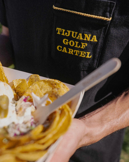 Detail of a black t-shirt with yellow embroidered Tijuana Golf Cartel text on the chest pocket.
