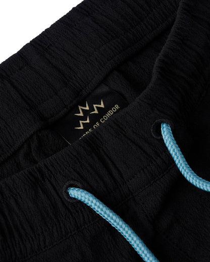 Detail of black shorts featuring a contrast light blue drawstring and an elastic waistband with a label.