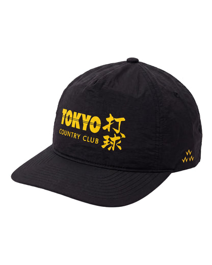 Black nylon snapback featuring bold yellow Tokyo Country Club lettering and Japanese characters on the front.