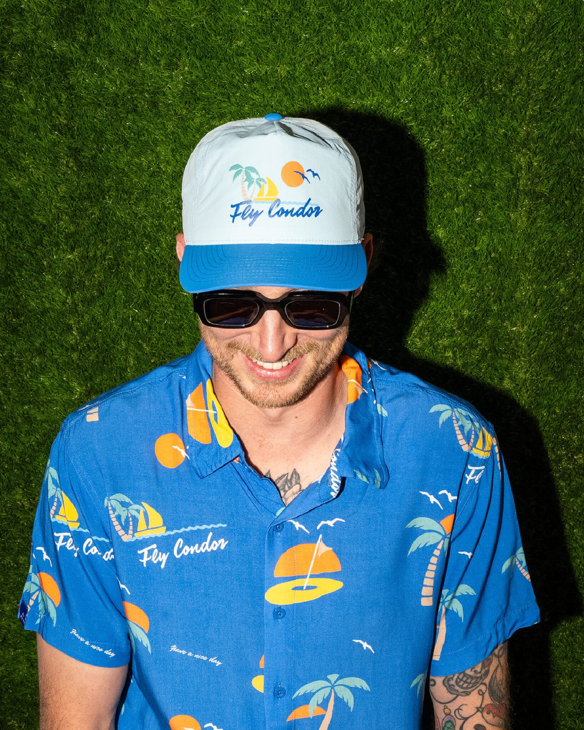 A person wearing a blue short-sleeve shirt with a yellow and white palm tree graphic and matching cap.
