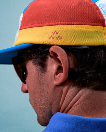 A man wearing a multi-colour athletic cap with a yellow band, red crown, and a printed logo design.