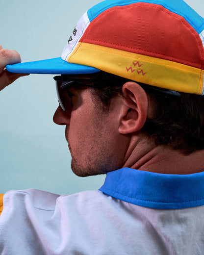 A man wearing a multi-colour athletic sports cap with a printed front and a blue flexible brim.