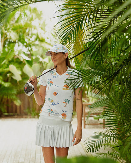 A woman outdoors wearing a white 5 panel strapback hat with a matching patterned tee and pleated skirt.