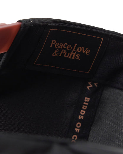 Detail of a black snapback cap featuring an interior label with Peace, Love & Putts text and a red strap.
