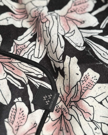 Detail of an azalea pink and black golf towel with an all-over floral print and a small black label.