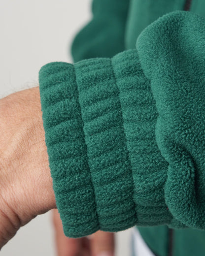 Detail of the ribbed elastic cuff on a green polar fleece sweater worn around a person's wrist.