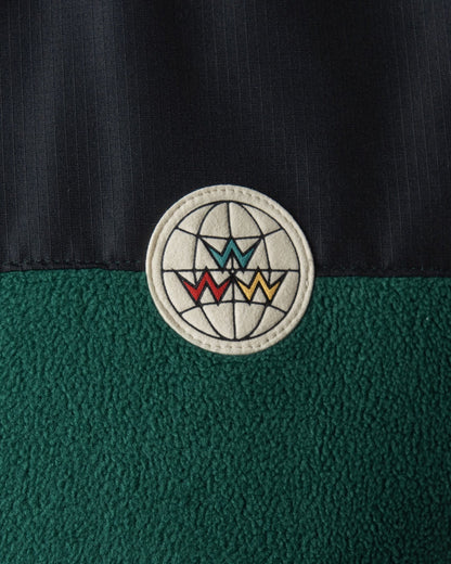 Detail of an Amazon green fleece jacket with a black shoulder panel and a round globe patch.