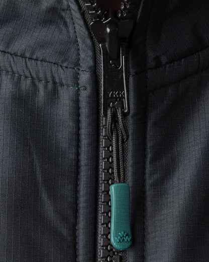Detail of an amazon green fleece jacket with a black ripstop shoulder panel and a rubber zip puller.