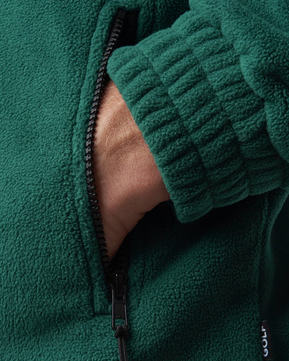 Detail of an amazon green fleece sweater featuring a black zipper pocket and ribbed cuff.