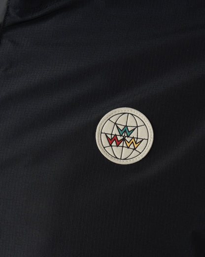 Detail of a black rain jacket featuring a circular pleather patch with a globe and colorful W design.