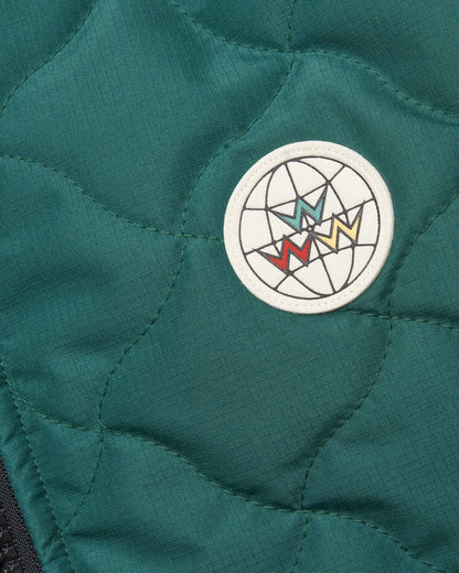 Detail of an amazon green vest with warped argyle quilting and a round globe patch.