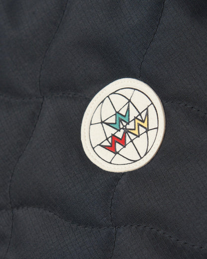 Detail of a black quilted vest featuring a round white pleather patch with a globe and zig-zag motif.
