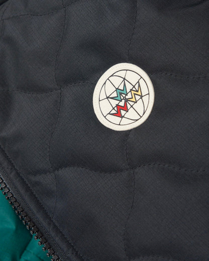 Detail of a black reversible vest with warped argyle quilting and a round logo patch.