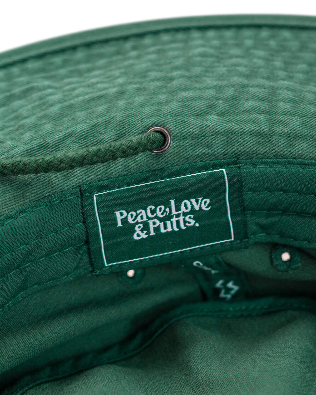 Detail of a green boonie hat featuring a tonal drawcord through a brass eyelet and an interior logo label.