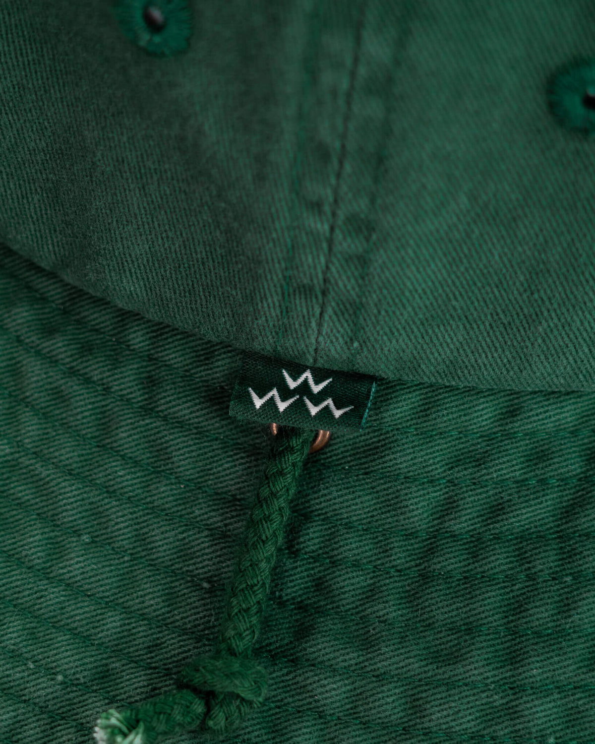Detail of a green cotton boonie hat showing a small logo tag and a tonal drawcord.