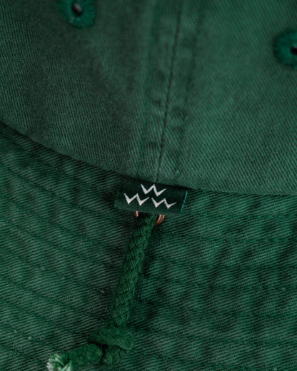 Detail of a green cotton boonie hat showing a small logo tag and a tonal drawcord.