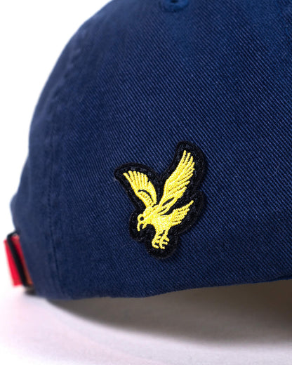 Detail of a navy cotton cap featuring an embroidered yellow bird logo on the side panel.