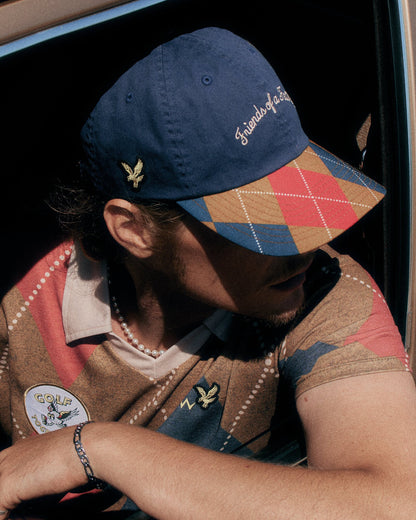 A man wearing a navy cap with embroidered script and an argyle brim, plus a matching argyle polo shirt.