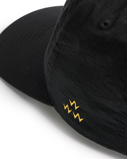 Detail of a black nylon snapback with a yellow embroidered logo design on the side panel and curved brim.