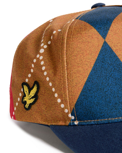 Detail of an argyle snapback with a navy brim, featuring a yellow bird logo embroidered on the side.