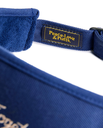 Detail of a navy visor with an embroidered Peace, Love & Putts. patch and adjustable metal buckle.
