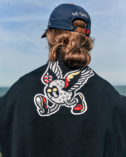 Back of a person wearing a black crewneck knitted sweater featuring a winged golf ball intarsia design.