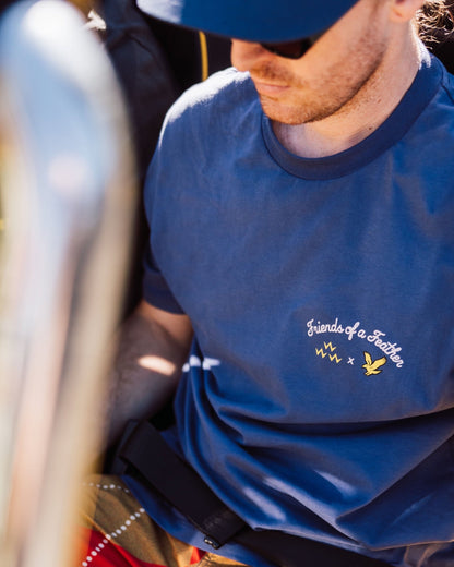 A man wearing a crown blue t-shirt featuring printed Friends of a Feather chest graphics.