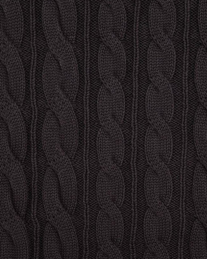 Detail of a black cotton vest with a vertical cable knit texture and ribbing.