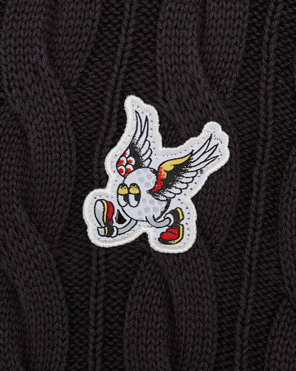 Detail of a black cable knit vest featuring an embroidered winged golf ball badge with arms and legs.