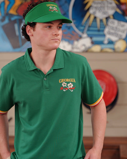 A man wearing a green polo shirt with tri-colour sleeve cuffs and an embroidered chest logo, and a matching visor.