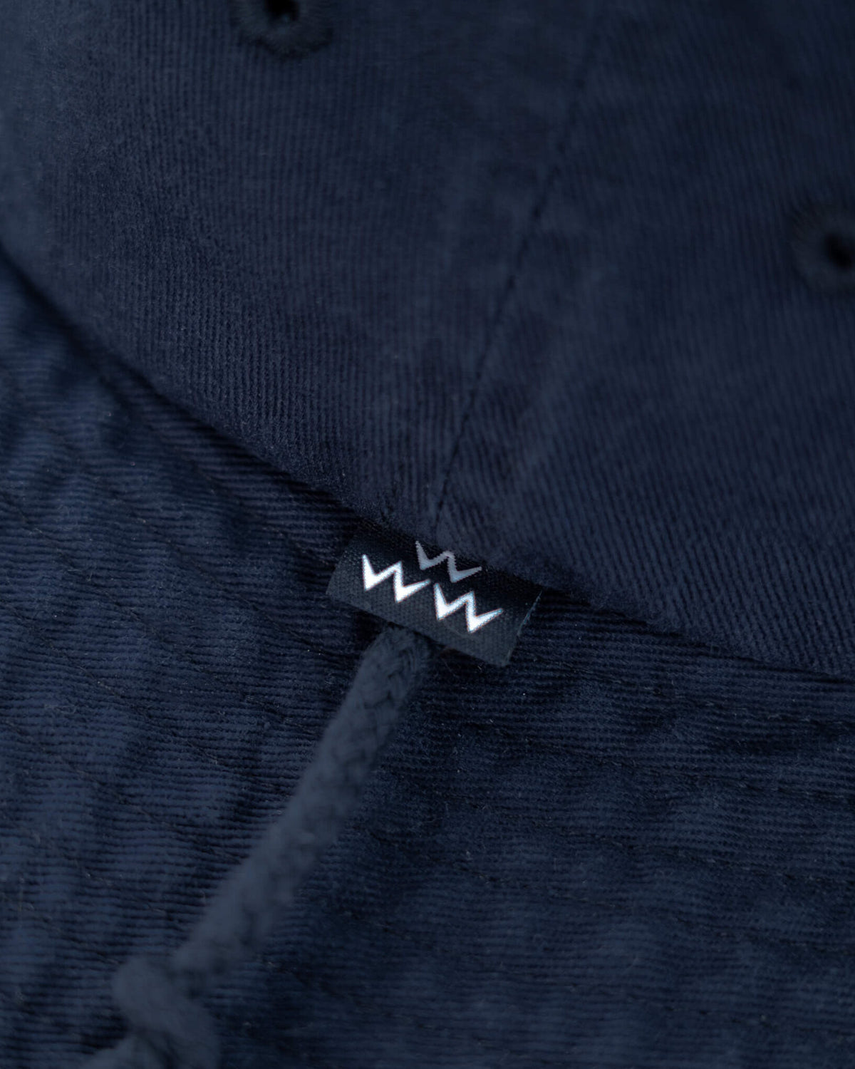 Detail of a navy cotton boonie hat showing a tonal drawcord and a small black and white logo label.