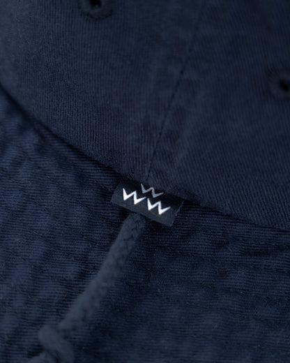 Detail of a navy cotton boonie hat showing a tonal drawcord and a small black and white logo label.