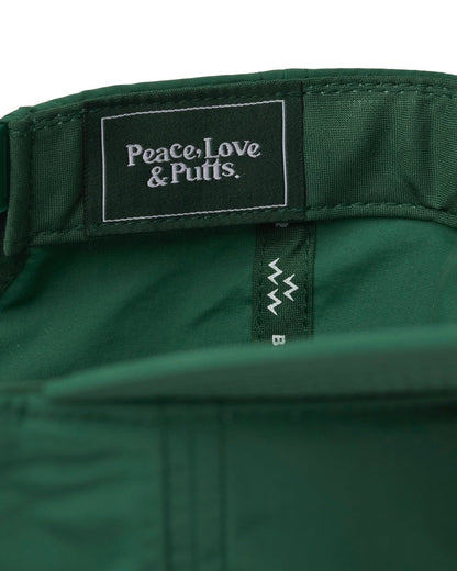 Detail of the green snapback's interior, showing a woven label with text reading Peace, Love & Putts.