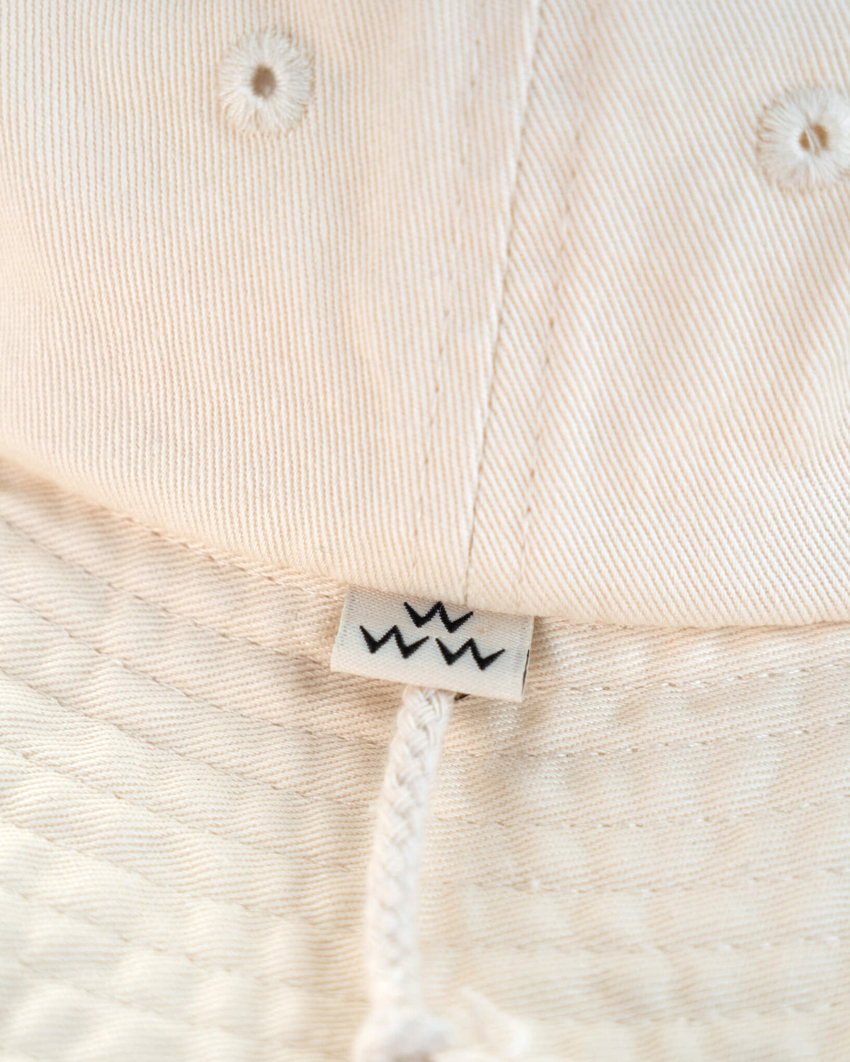 Detail of an off-white cotton boonie hat featuring a small branded label and drawcord.