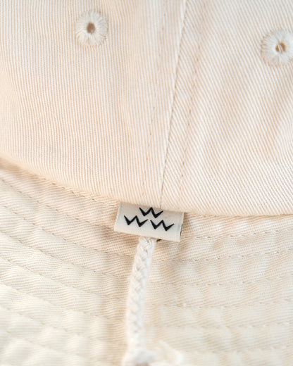 Detail of an off-white cotton boonie hat featuring a small branded label and drawcord.