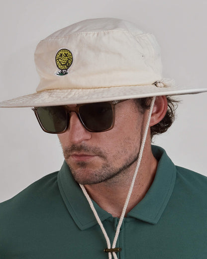 A man wearing an off-white cotton canvas boonie hat with a yellow smiley face golf ball graphic.