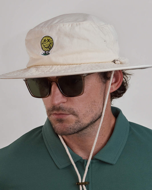 A man wearing an off-white cotton canvas boonie hat with a yellow smiley face golf ball graphic.
