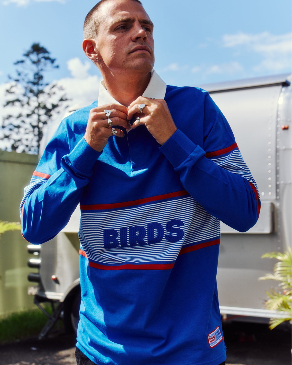 A man wearing a blue cotton sweater with a white collar, striped chest panel, and embroidered lettering.