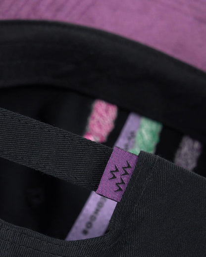 Detail of a black cap with a purple strap and back buckle, showing signature inner taping.