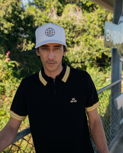 A man wearing a black knit polo with a quarter zip, striped yellow collar and sleeve cuffs.
