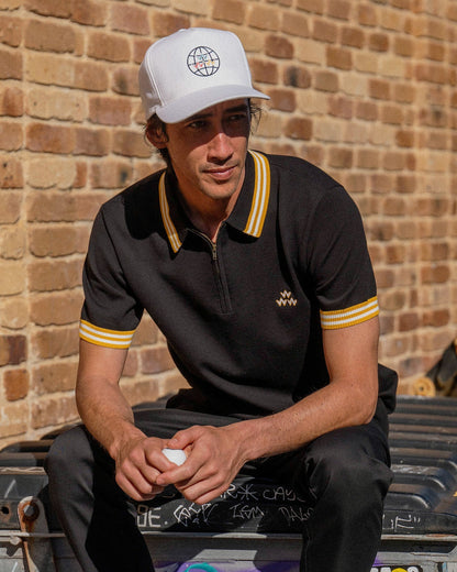 A man wearing a black knit polo shirt featuring a quarter-zip, yellow and white collar trim.
