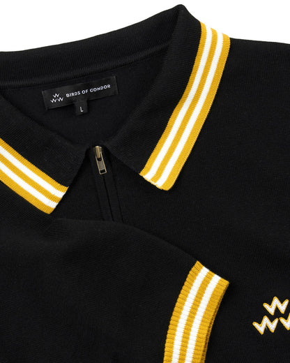 Detail of a black knit polo shirt featuring a quarter-zip, contrast yellow-and-white collar, and a triple eagle logo.